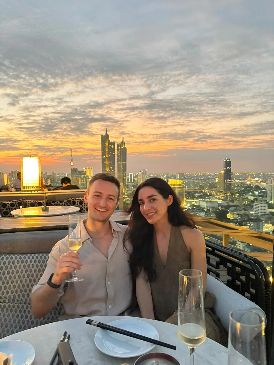 Jay and Lily together at dinner, with the sunset behind them