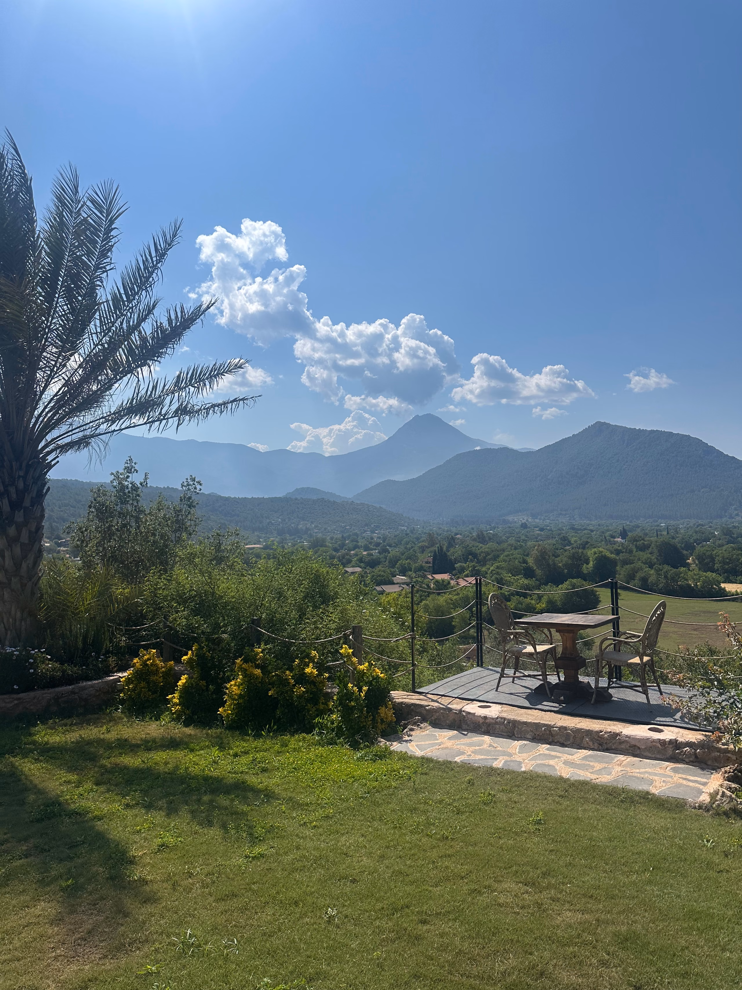 The Kayaköy valley: mountains under tall cloud, with palms and planting in the foreground.